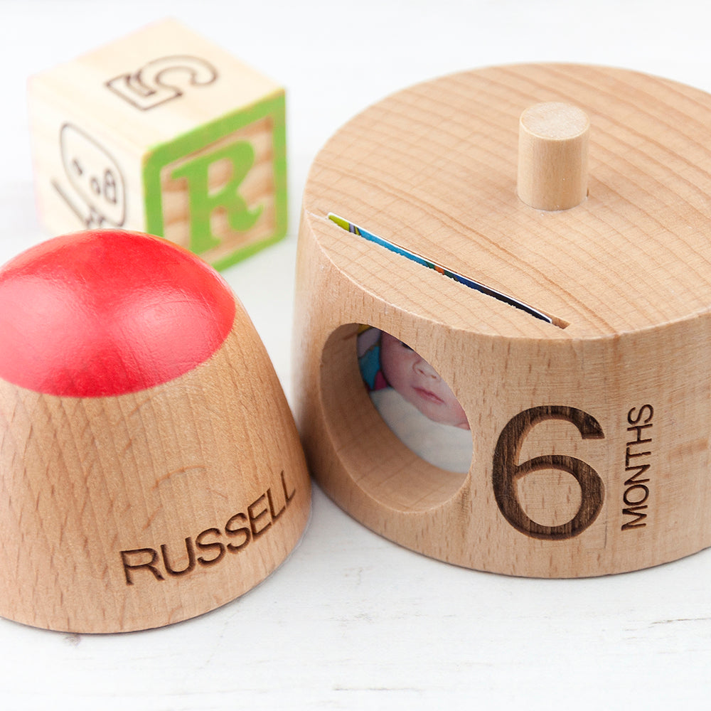 Wooden baby milestone toy with '6 months' marking and a red top, alongside a block with letter 'R'.