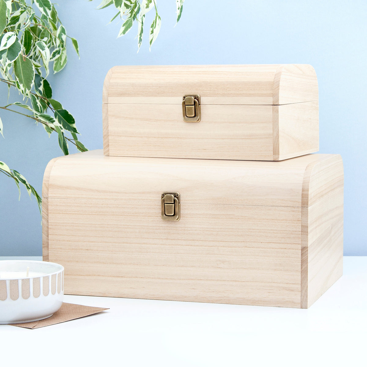 Two beige wooden storage boxes with gold latches on a light blue background.
