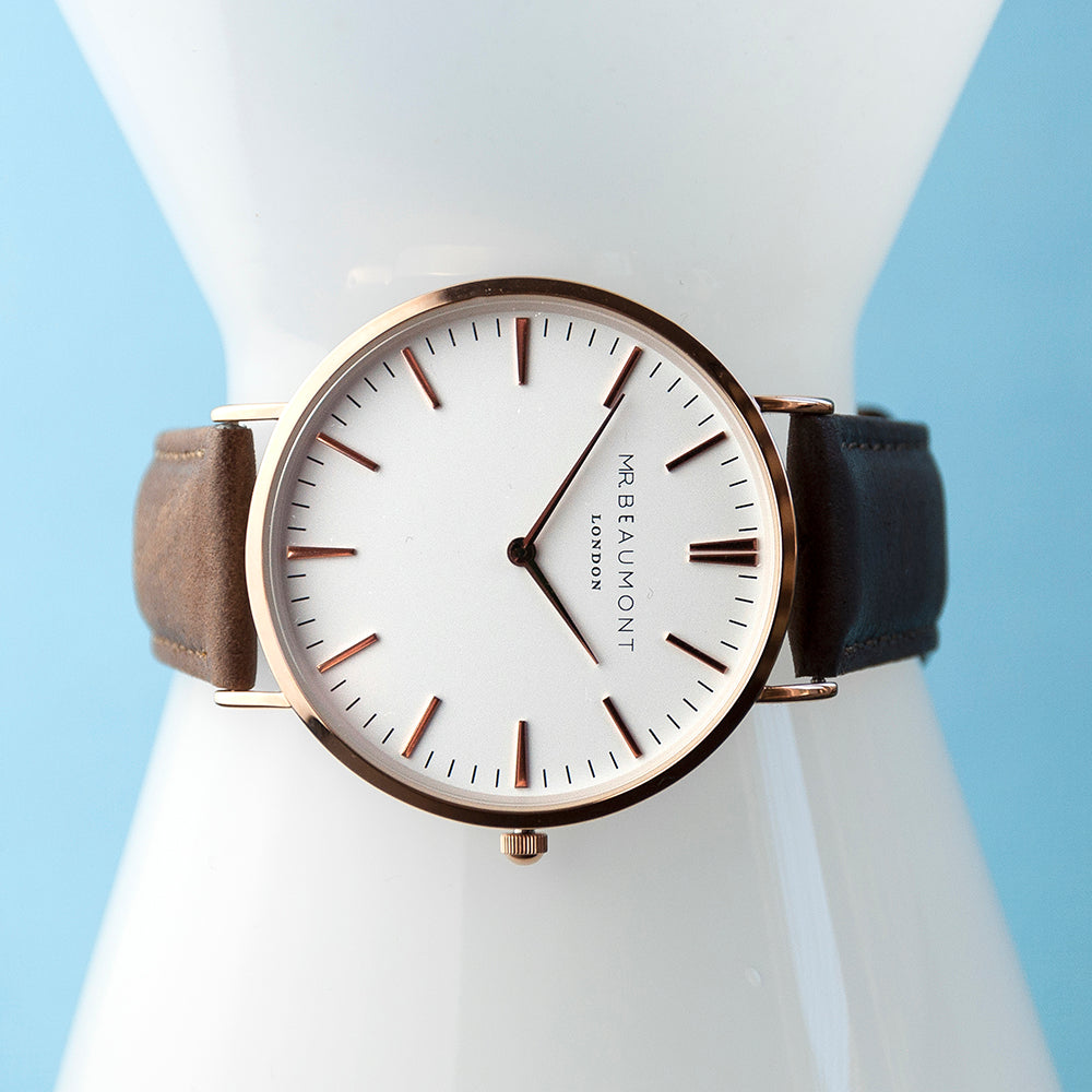 Watch with a brown strap and rose gold case on a white mannequin against a light blue background