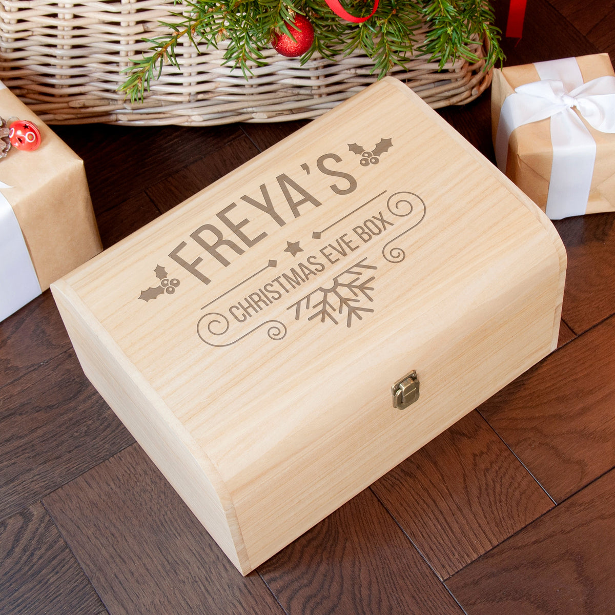 Wooden Christmas Eve box with engraved name on a wooden floor with gift boxes and decorations.