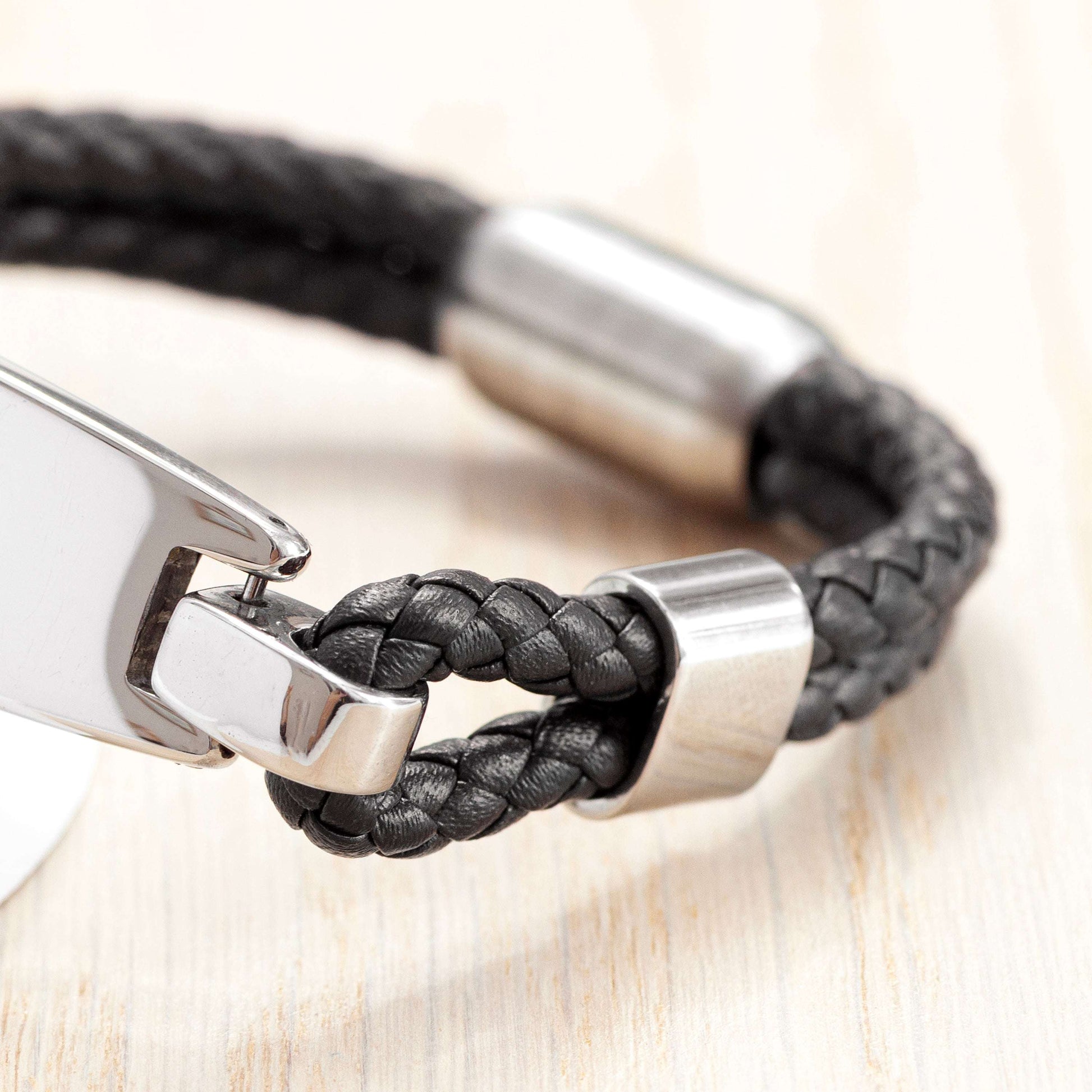 Black braided leather bracelet with silver clasp on a light wood surface