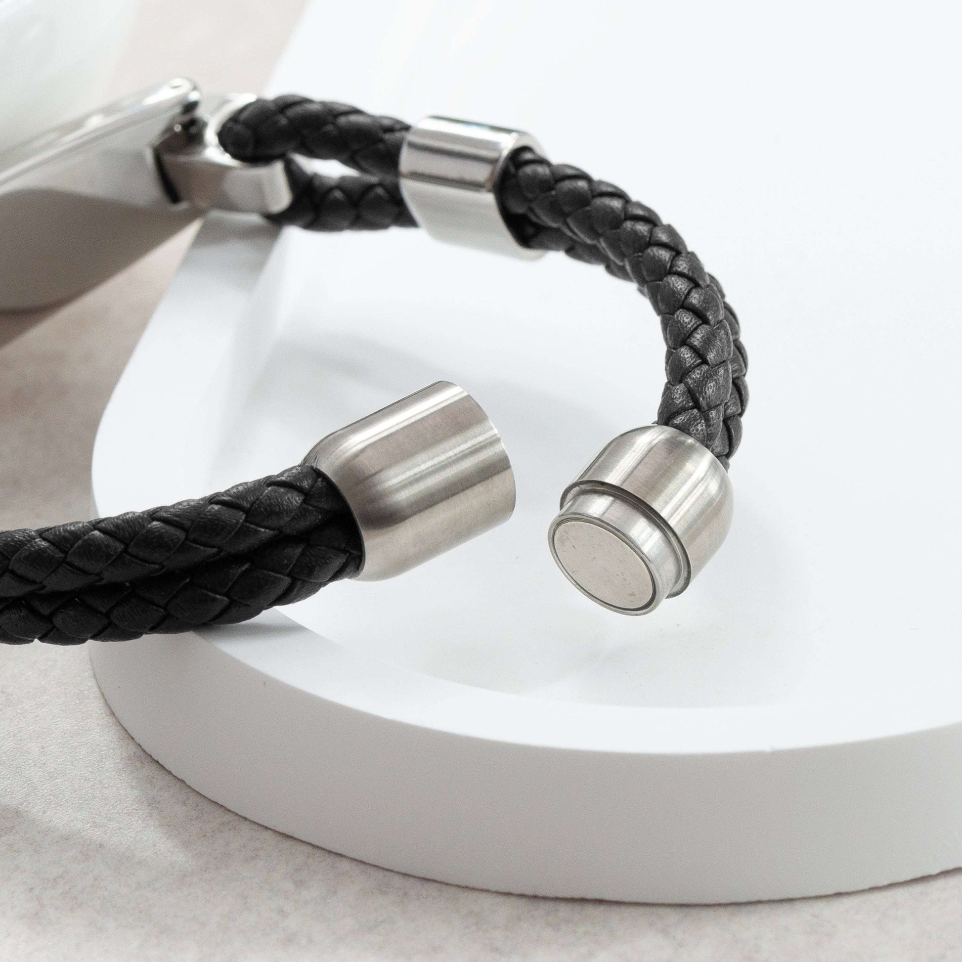 Black braided leather bracelet with silver metal clasps on a white background