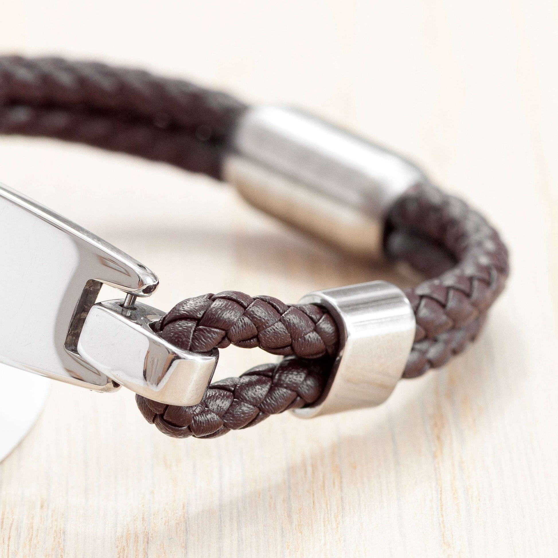 Brown braided leather bracelet with silver clasp on a light wooden surface
