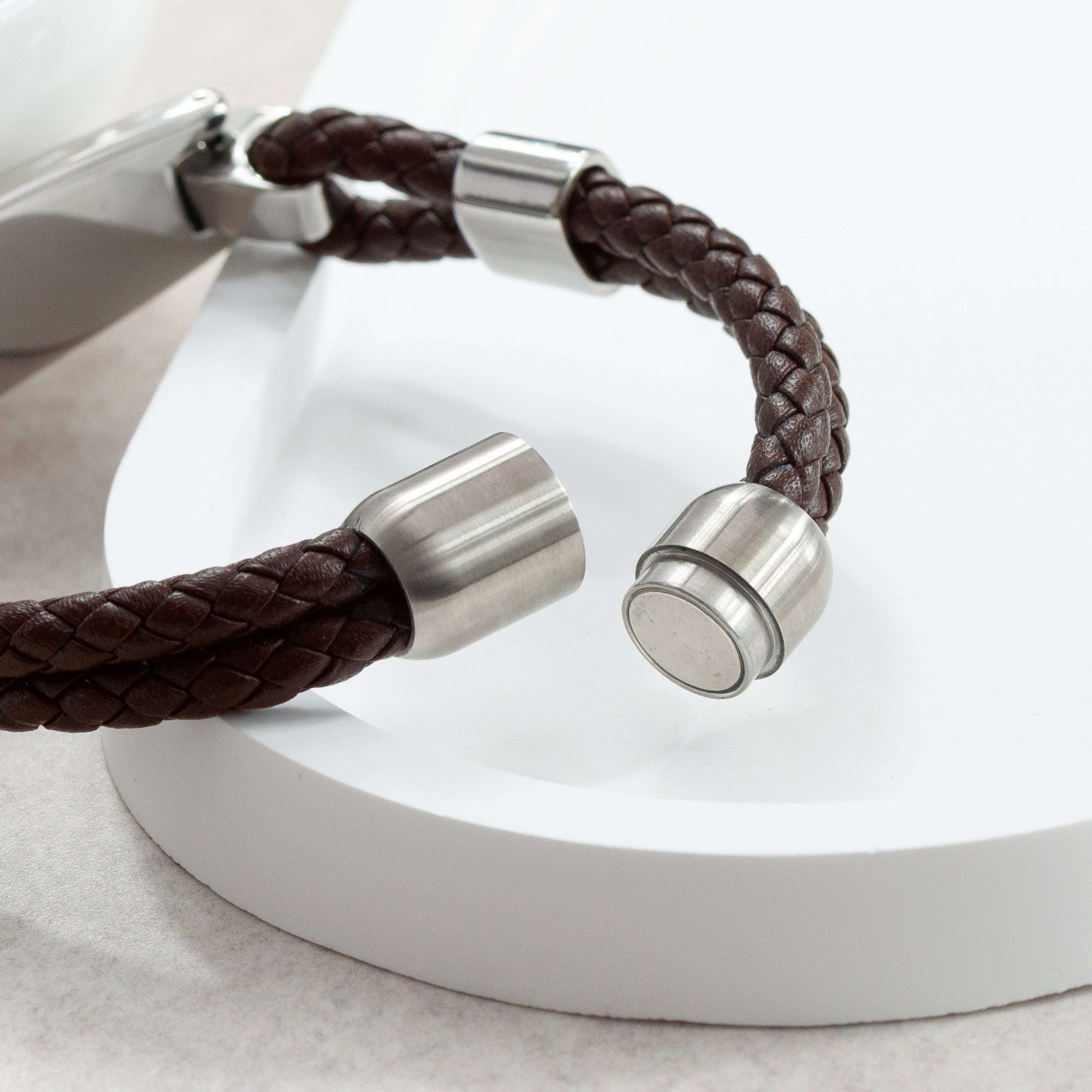 Brown braided leather bracelet with silver metal clasps on a white background