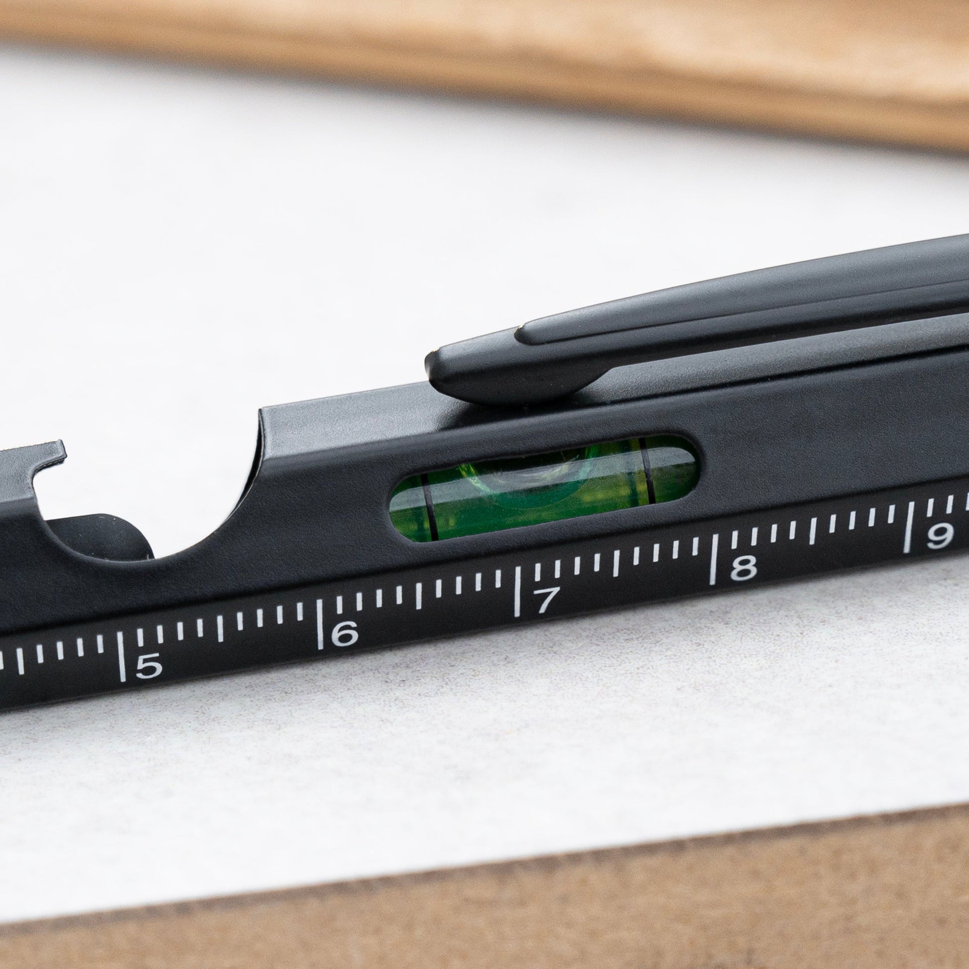 Close-up of a black personalized-carpenter's square ruler with a built-in level bubble and measurement markings, resting on a white surface.