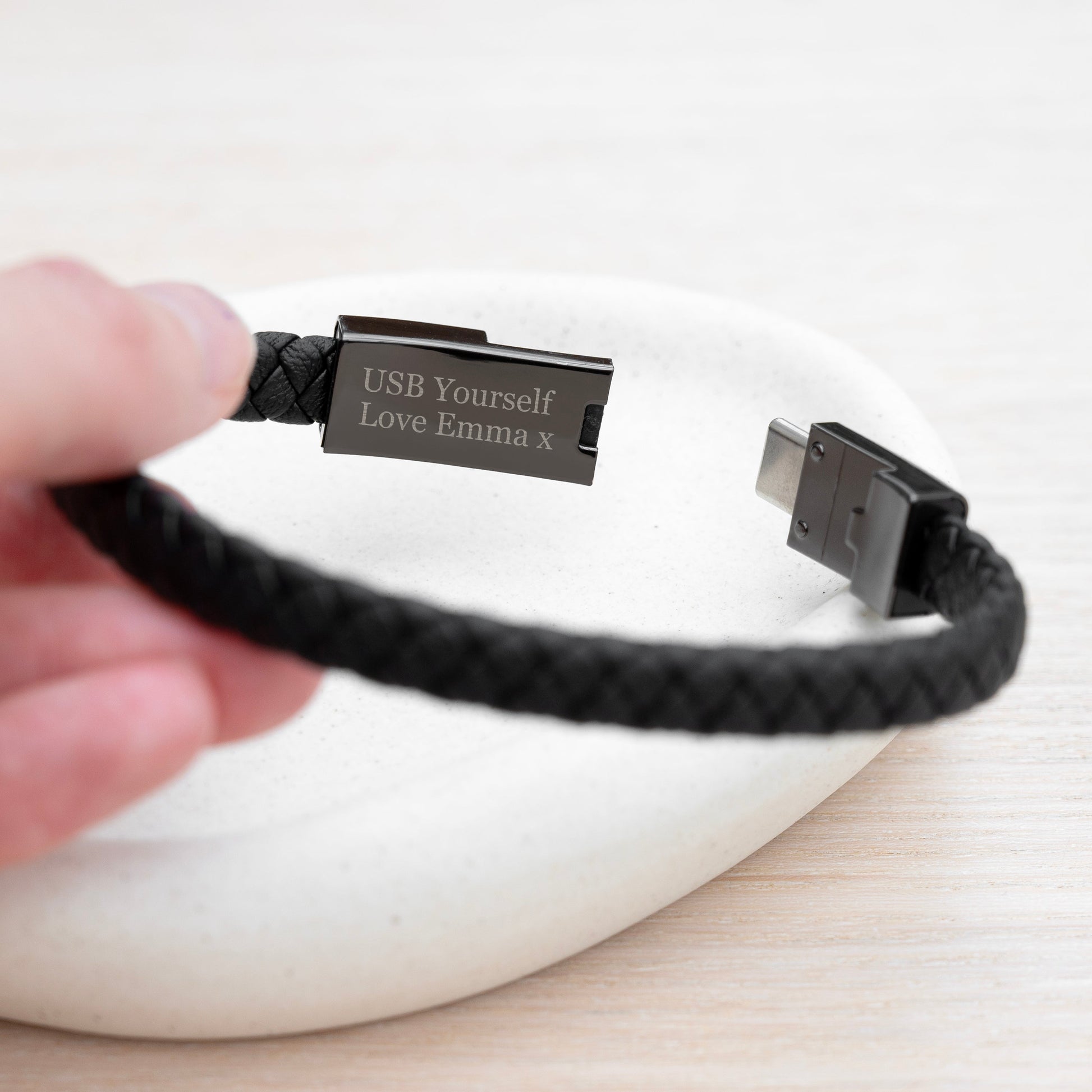 Black braided USB bracelet with engraved text held by a hand on a white background