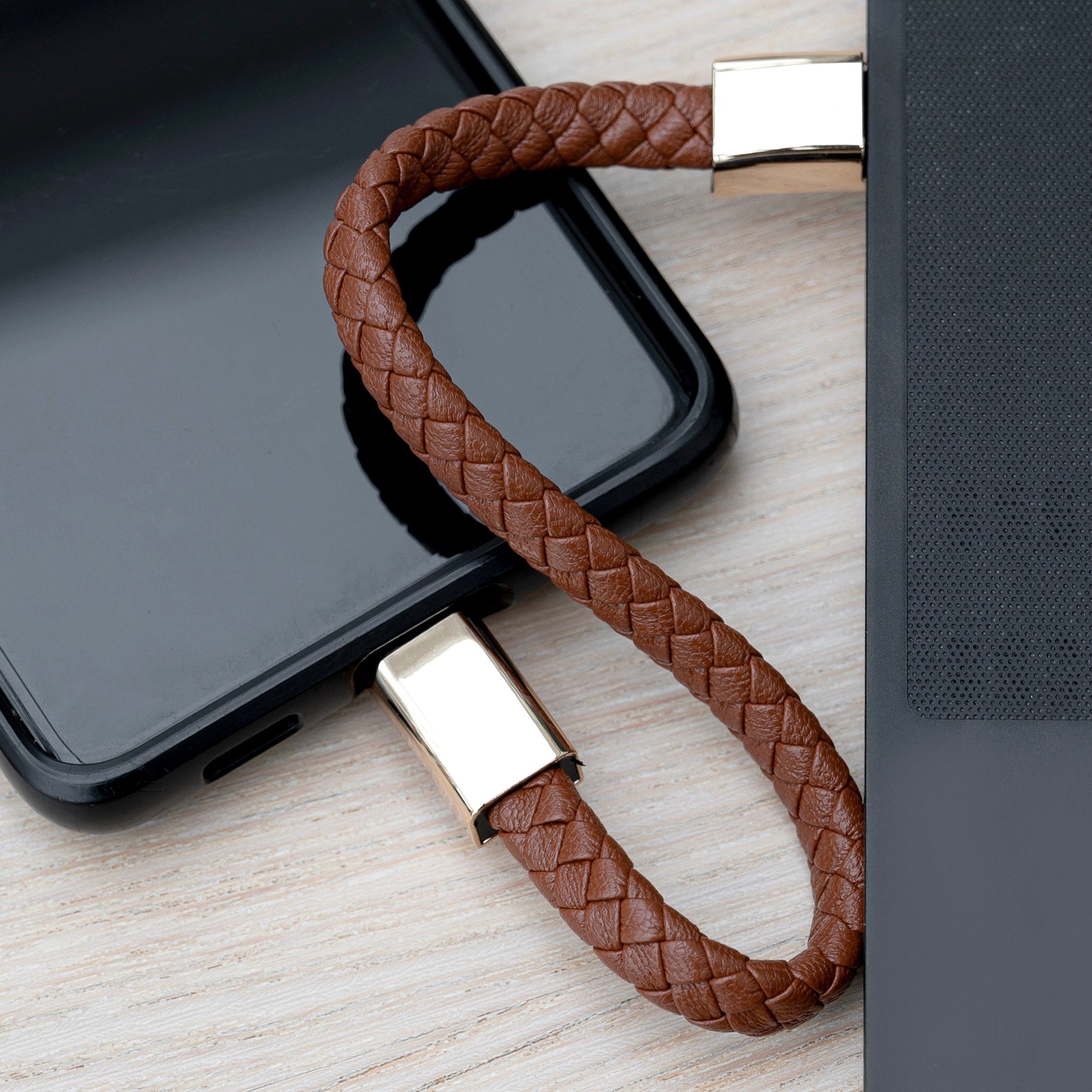 Brown braided USB cable-bracelet with gold connector on a wooden surface