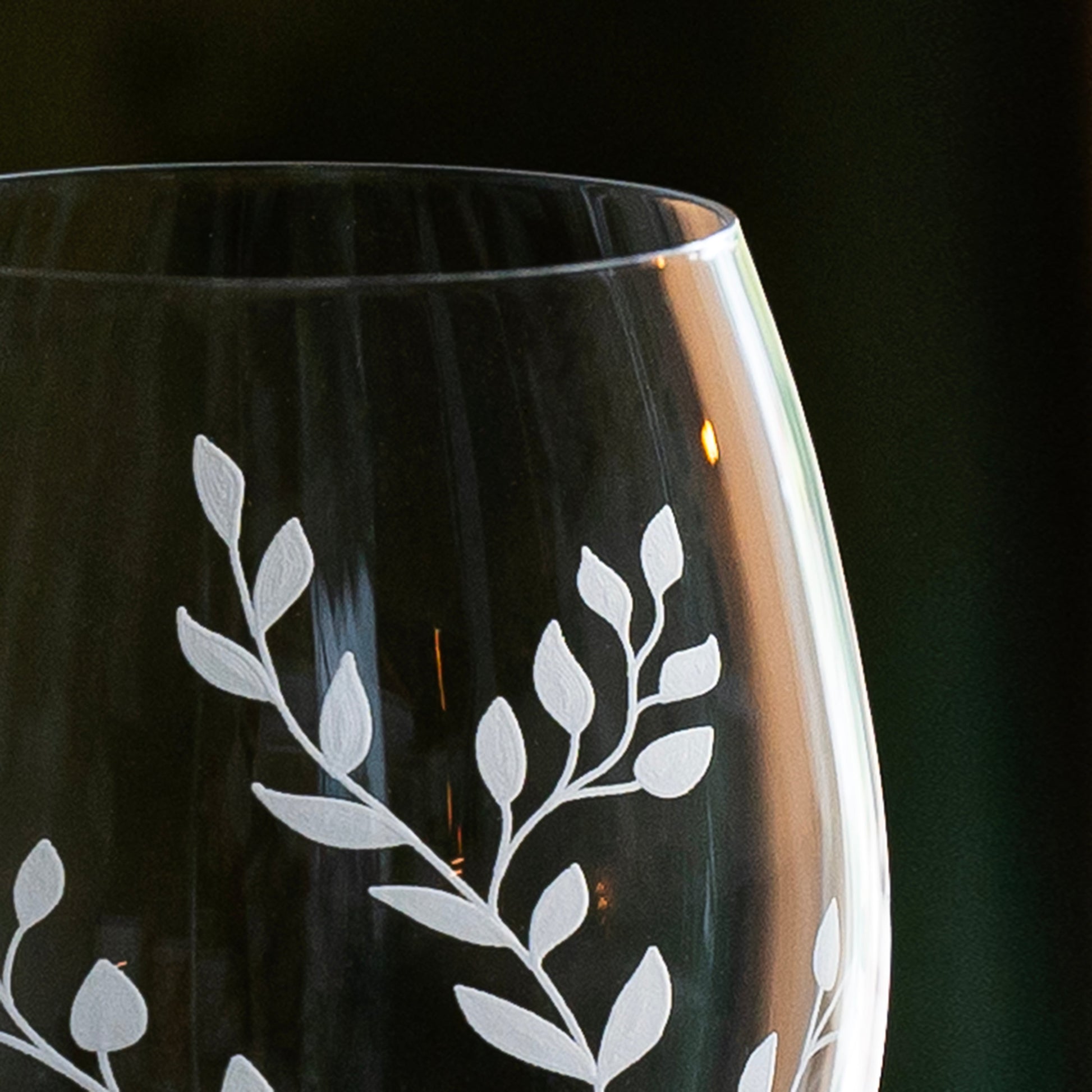 custom wine glass with white leaf etching on a dark background