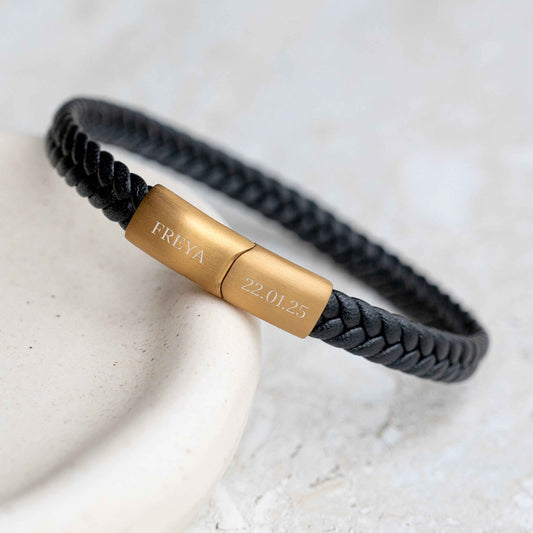 A black braided leather bracelet with a polished gold magnetic clasp engraved with name and the date