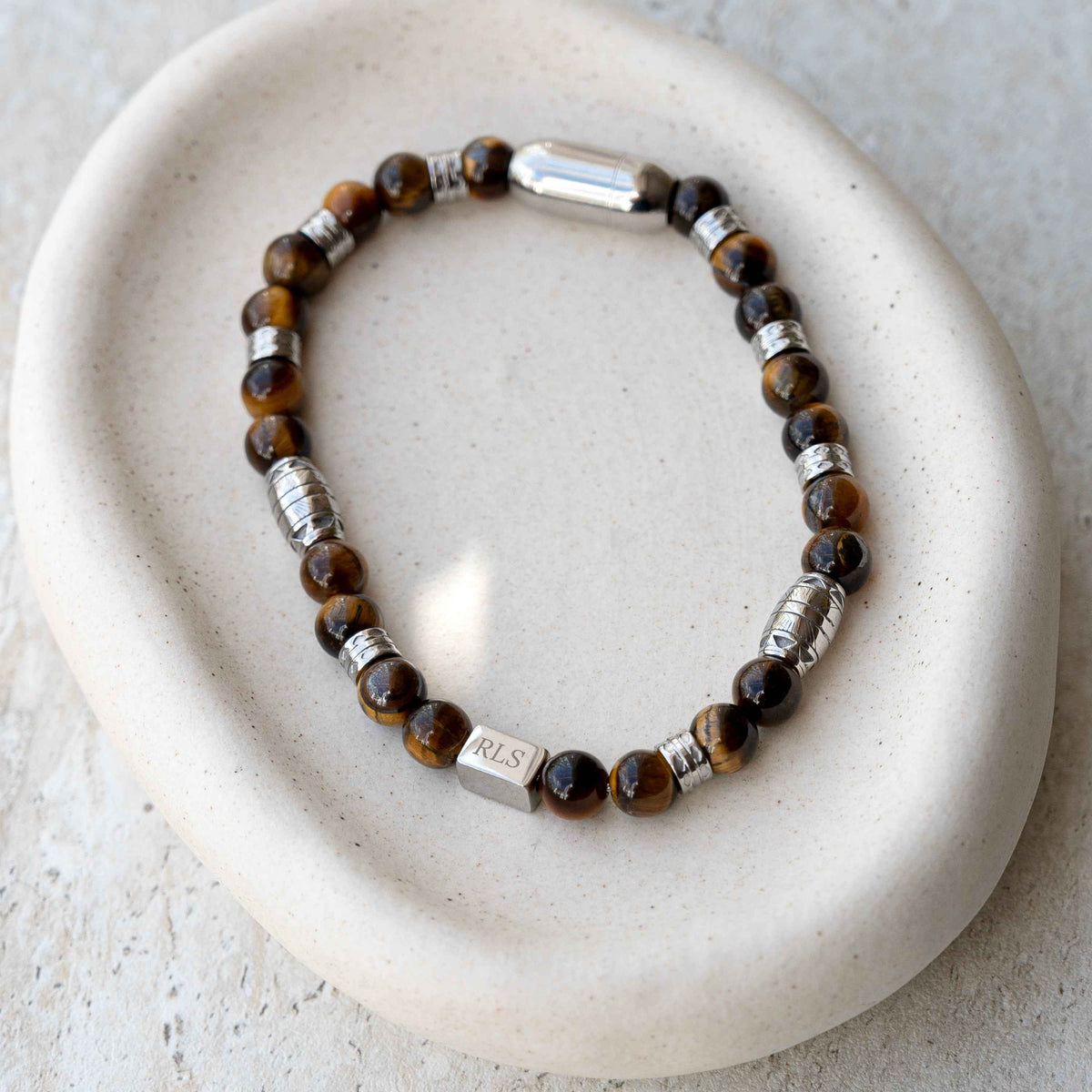 A beaded stretch bracelet with brown and black tiger's eye beads and silver spacer beads, engraved with initials.