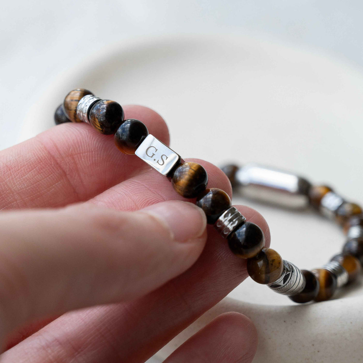 Personalized Gemstone Bead Bracelet  made of brown and black tiger's eye beads with silver spacer beads and a silver rectangular charm engraved with initials.
