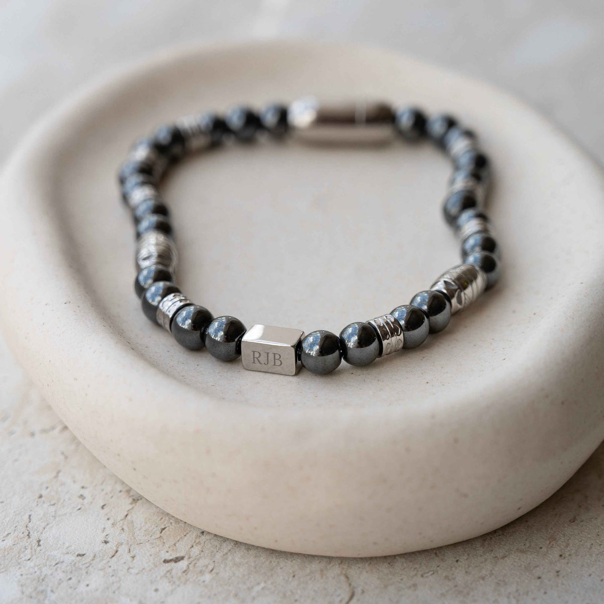 A Personalized Hematite-Gemstone Bead Bracelet bracelet, featuring a silver cube charm engraved with initials