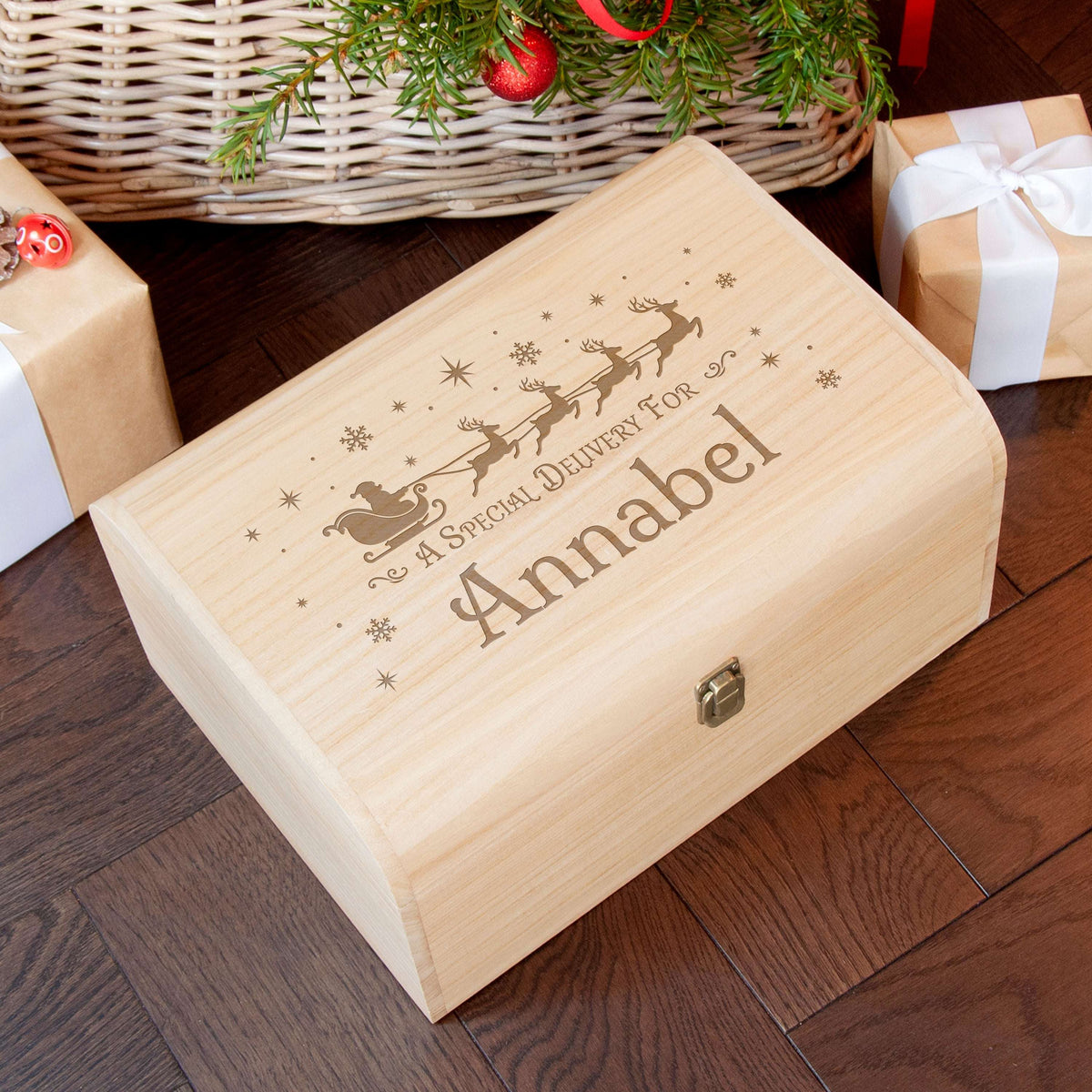 Personalized-Wooden Christmas Eve box with engraved name on a wooden floor with gift boxes and decorations.