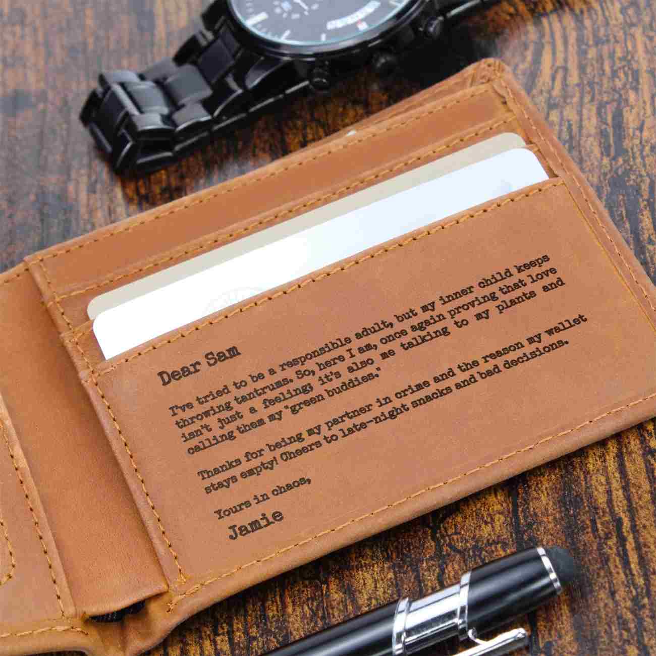 A close-up of a brown leather wallet with a personalized engraved message on the front pocket, shown open with cards inside on a wooden surface. A black watch and pen are partially visible around it.