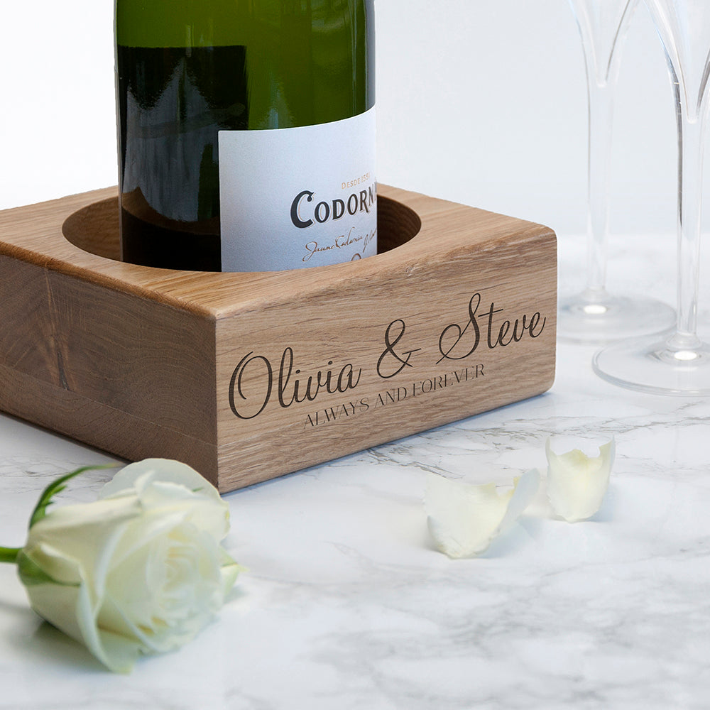 Wooden wine bottle holder with engraved names 'Olivia & Steve' on a marble surface with a rose and candle.