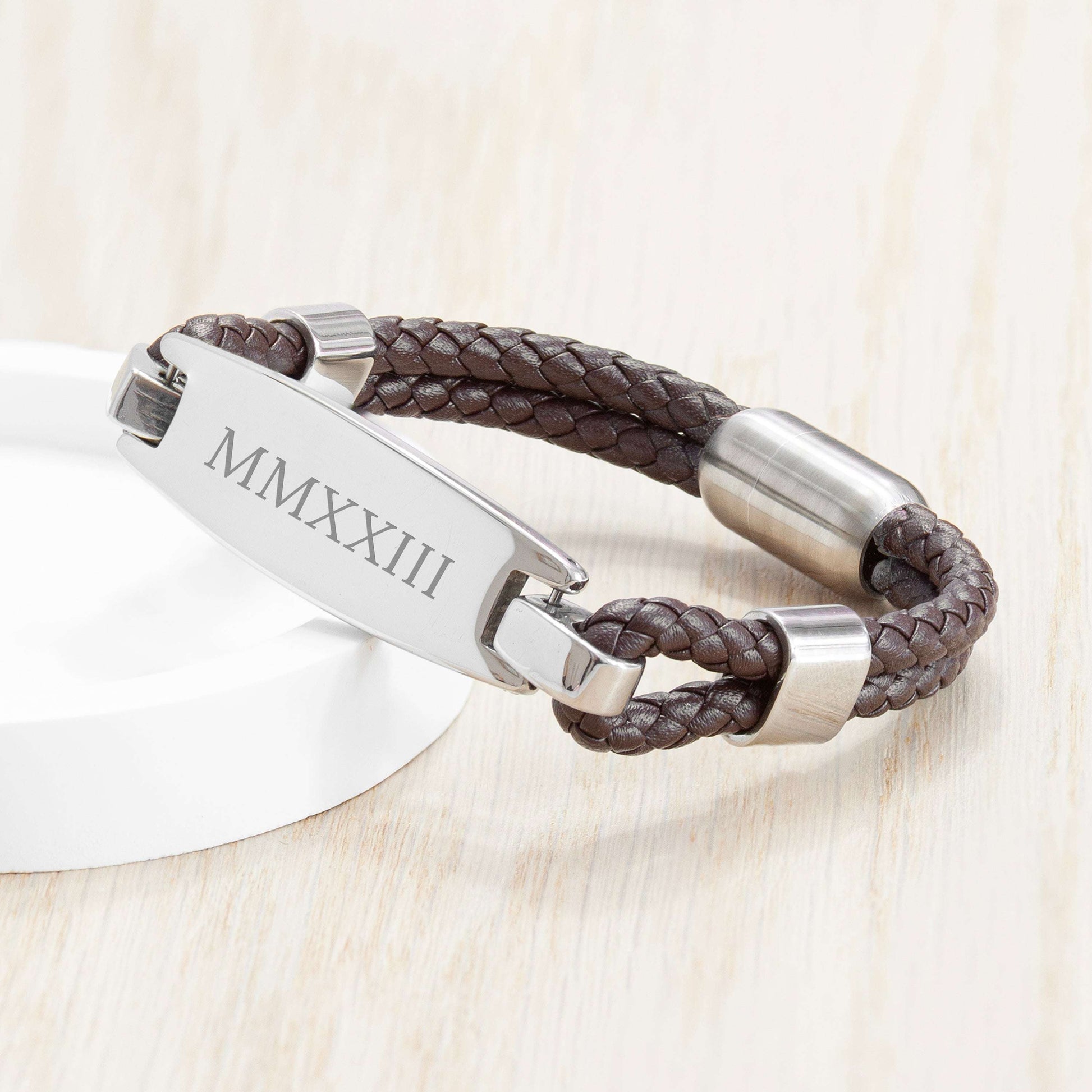 Brown braided leather-Mens- ID-bracelet with silver tag on a light wooden surface