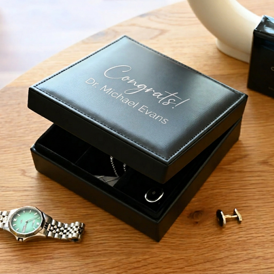 Black jewelry box with 'Congrats! Dr. Michael Evans' text, watch on wooden surface