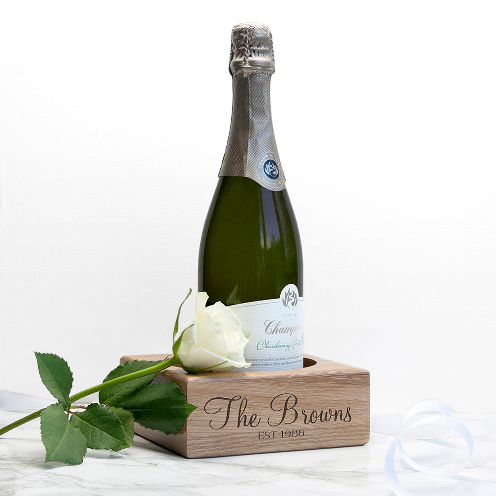 Bottle of champagne with a white rose on a wooden coaster with 'The Browns' engraving.