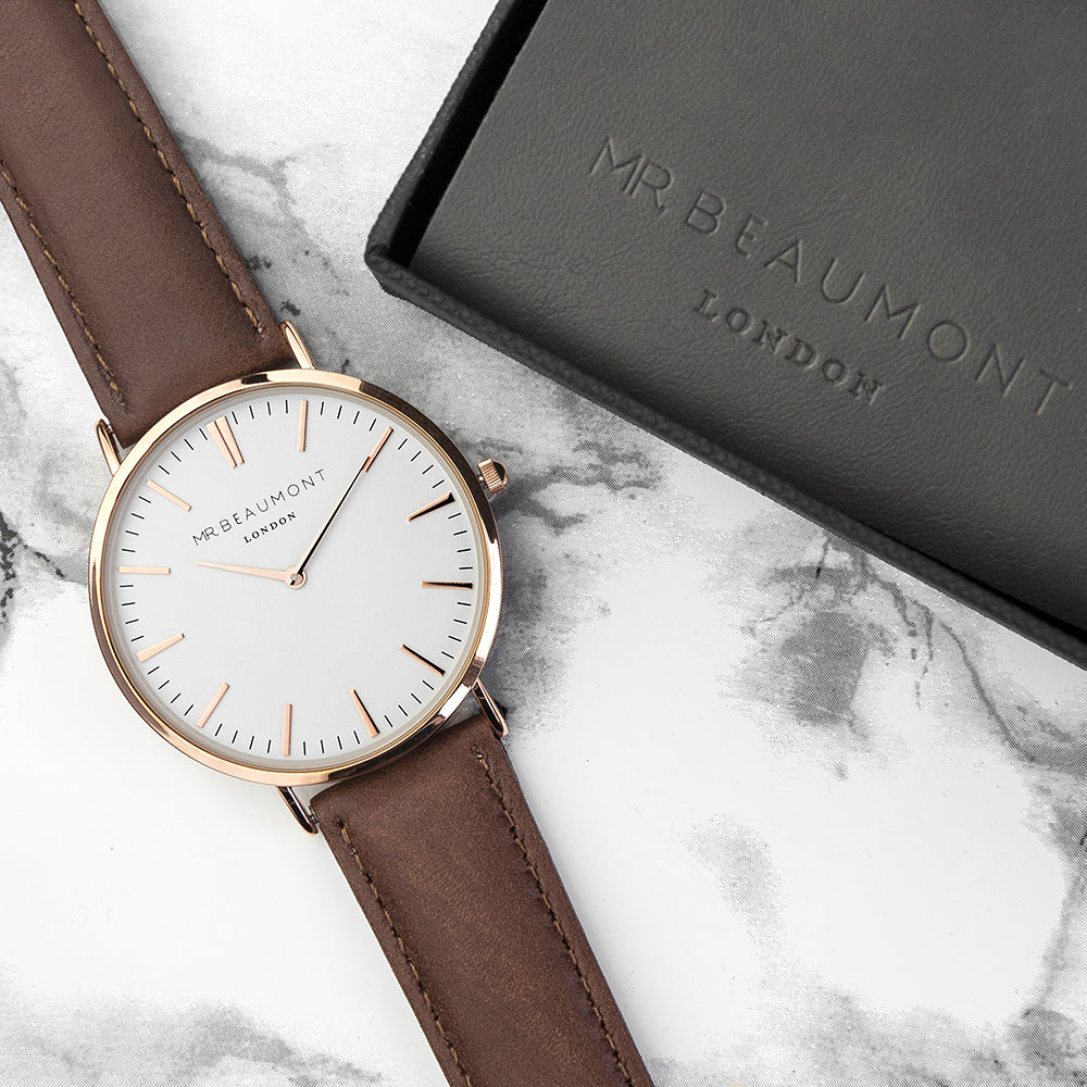 Watch with brown strap and gold case on marble surface with 'MR BEAUMONT LONDON' packaging.